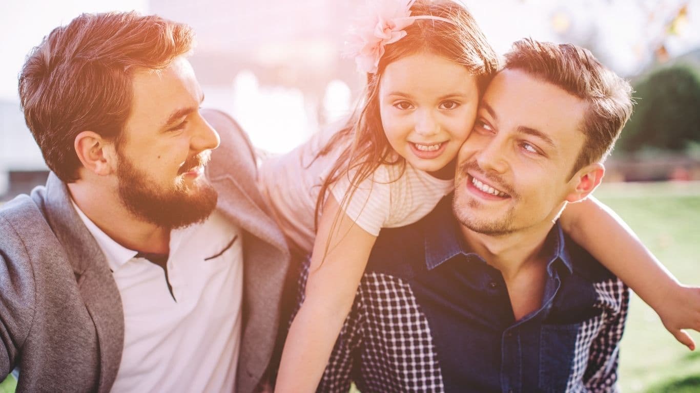 Ein Kind sitzt zwischen zwei Erwachsenen, die sich lächelnd ansehen.