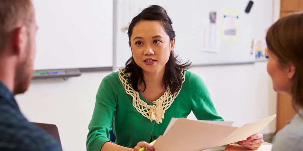 Erwachsene Person sitzt an einem Tisch und hält Unterlagen in der Hand.