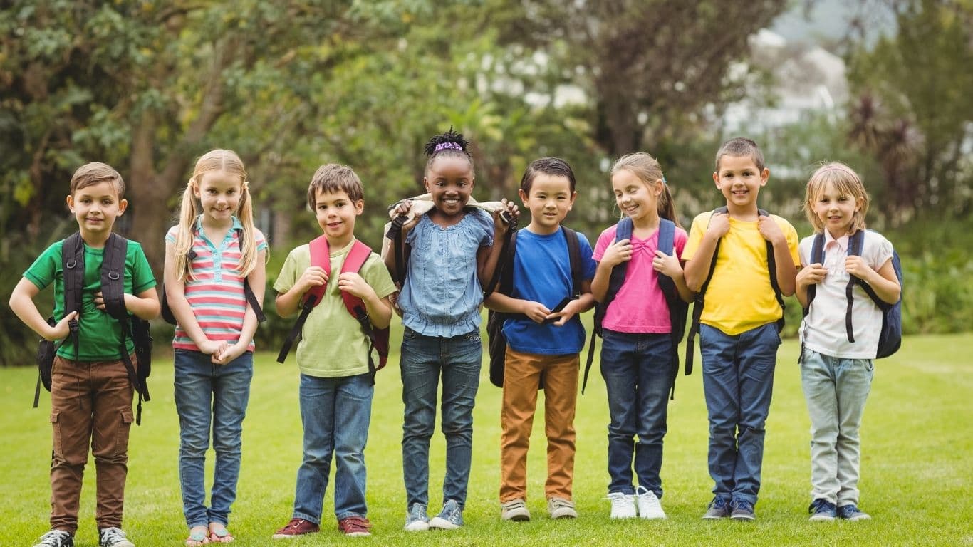 Acht Kinder stehen auf einer Wiese mit ihren Schulranzen