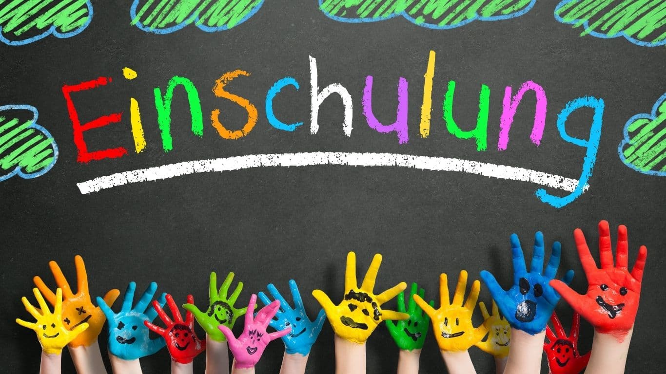 Bunt bemalte Hände vor einer Tafel mit der Aufschrift "Einschulung"