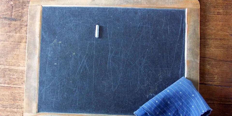 Schwarze Schultafel mit Kreide und Tafelschwamm.