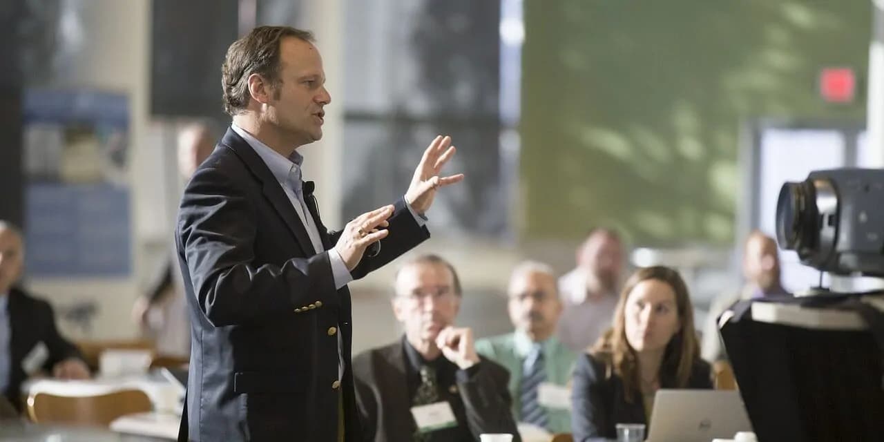 Erwachsene Person steht vor einer Gruppe und hält einen Vortrag.