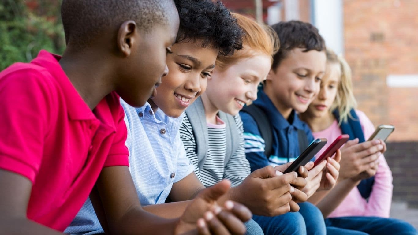 Kinder sitzen nebeneinander und schauen gemeinsam auf ihre Smartphones.