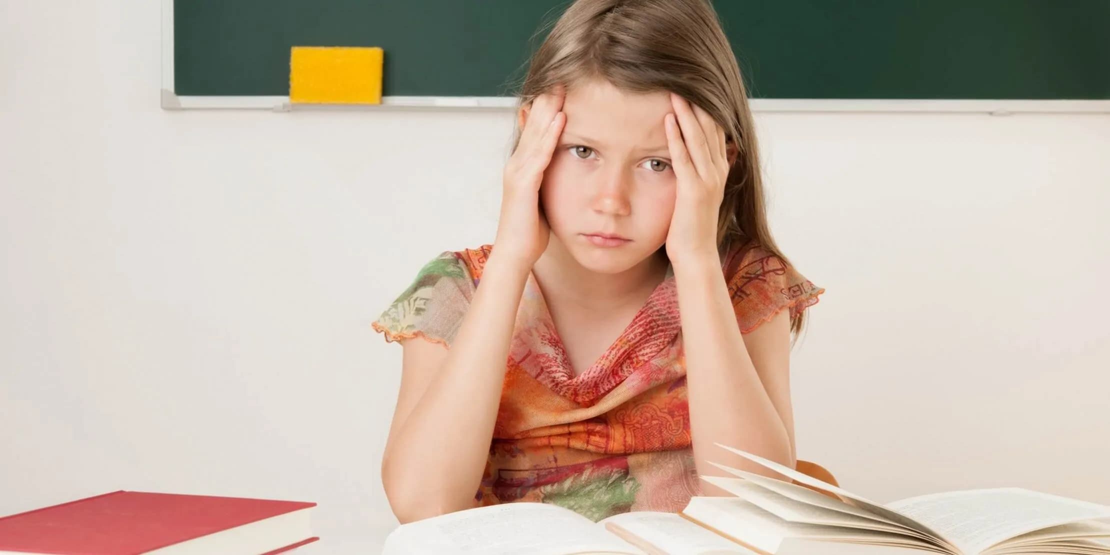 Kind sitzt am Tisch vor aufgeschlagenen Schulbüchern.