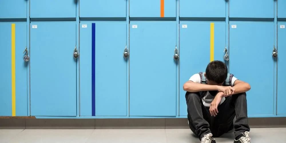 Kind sitzt allein vor einer Reihe von Schließfächern.